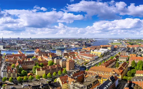 Panorama von Kopenhagen mit roten Dächern und Wasserblick bei bewölktem Himmel.