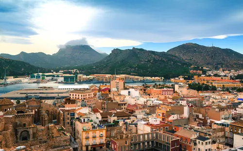 Stadtansicht mit Bergen und Hafen im Hintergrund bei bewölktem Himmel.