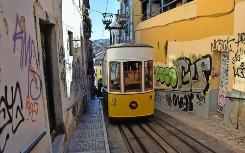 Gelbe Straßenbahn fährt durch enge, graffiti-bedeckte Gasse in einer Altstadt.