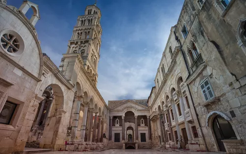 Historischer Innenhof mit alten Steingebäuden und Turm bei Sonnenschein.
