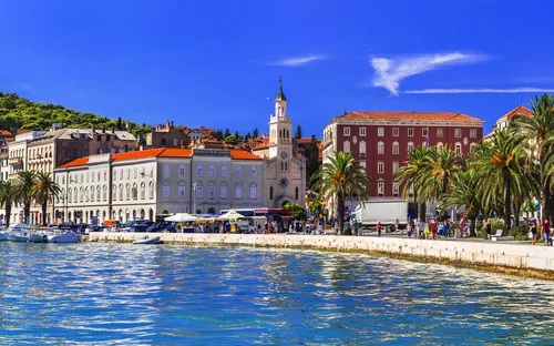 Küstenstadt mit Palmen, Gebäuden und blauem Himmel.