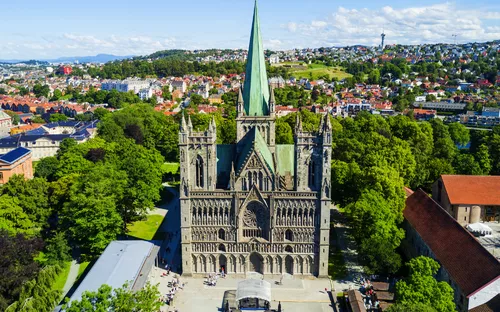 Luftaufnahme einer Kathedrale in einer Stadtlandschaft mit grünem Turm und vielen Bäumen.
