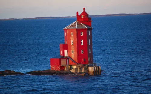 Roter Leuchtturm auf felsigem Eiland im blauen Meer.