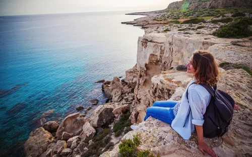 Frau mit Rucksack sitzt auf Felsen am Meer.