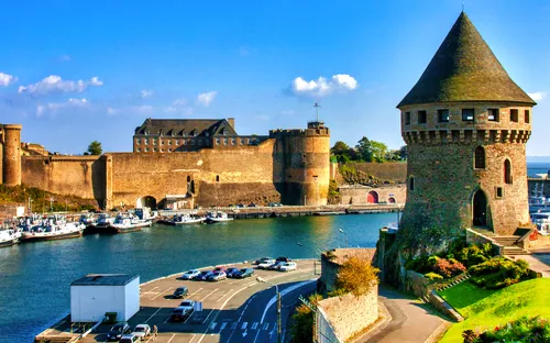 Historische Burganlage mit Hafen und Rundturm bei sonnigem Wetter.