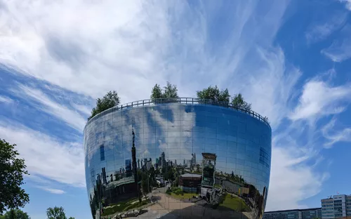 Modernes, rundes Gebäude mit spiegelnder Fassade und Bäumen auf dem Dach.