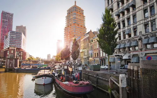 Stadtblick mit Fluss, Booten und modernen Gebäuden bei Sonnenuntergang.