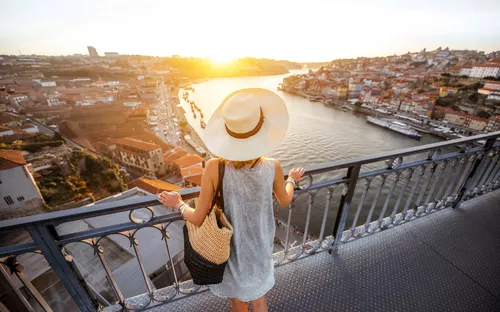 Frau mit Strohhut blickt auf Stadtpanorama bei Sonnenuntergang von Brücke aus.