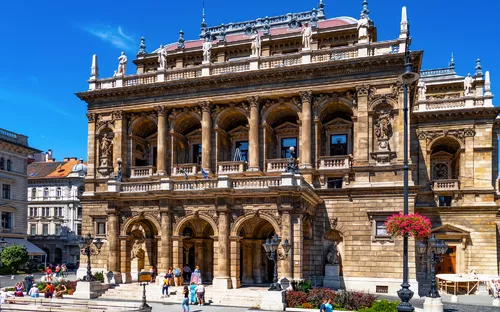 Historisches Opernhaus mit belebtem Vorplatz bei sonnigem Wetter.
