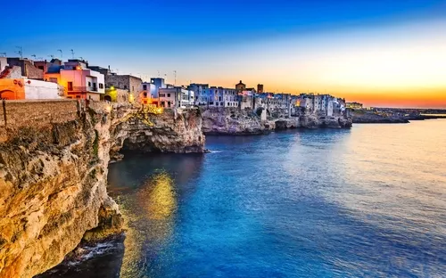 Küstenstadt bei Sonnenuntergang mit Gebäuden auf Klippen am Meer.