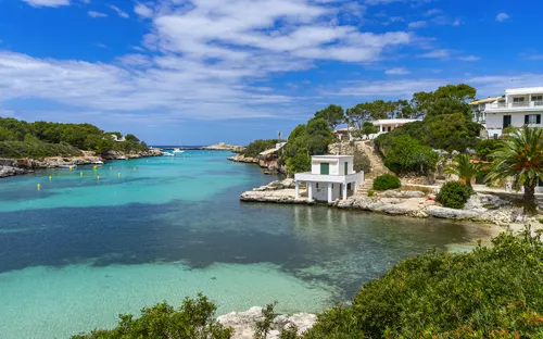 Küste mit klarem Wasser, Häusern und Bäumen unter blauem Himmel.