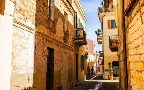 Enge Gasse mit alten Häusern und Balkonen unter blauem Himmel.