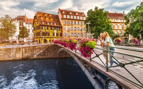 Stadtansicht mit Fachwerkhäusern und Menschen auf einer Brücke über einem Fluss.