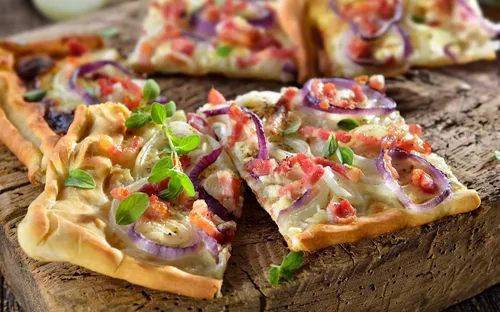 Flammkuchen mit Zwiebeln und Speck auf einem rustikalen Holztisch serviert.