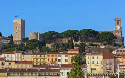 Historischer Gebäudekomplex mit Uhrturm und Bäumen hinter bunten Häusern.