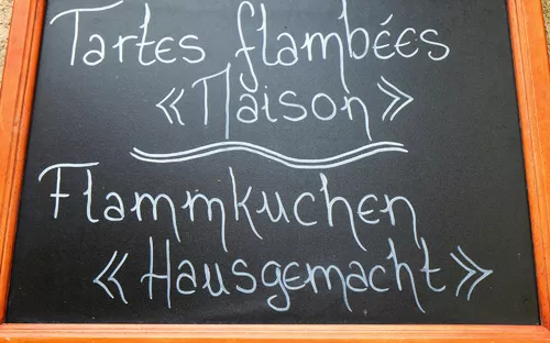 Tafel mit Aufschrift: Tartes flambées maison, Flammkuchen hausgemacht.