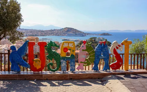 Kuşadası-Schriftzug aus bunten Buchstaben mit Meerblick im Hintergrund.