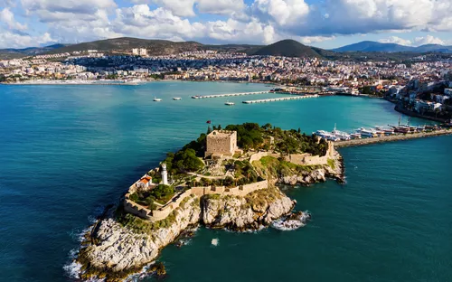 Insel mit historischem Gebäude und Leuchtturm im blauen Ozean, Stadt im Hintergrund