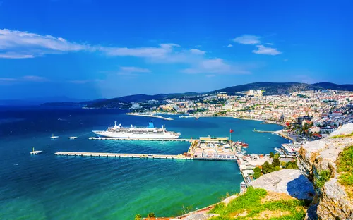 Küstenstadt mit Hafen und Kreuzfahrtschiff bei klarem Himmel.