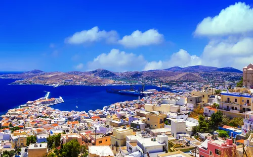 Stadtansicht mit Hafen und Kirche auf einem Hügel unter blauem Himmel.