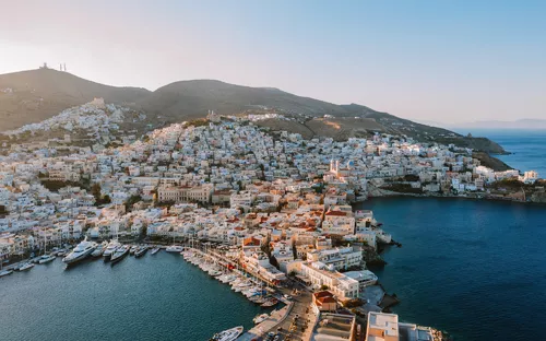 Küstenstadt mit Booten und Bergen im Hintergrund bei Sonnenuntergang.