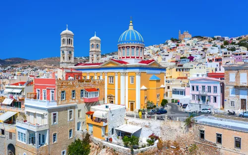 Bunte Stadt mit Kirchen und Kuppel auf Hügel unter blauem Himmel.