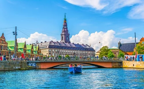 Menschen in einem blauen Boot auf einem Kanal vor historischem Gebäude an einem sonnigen Tag.