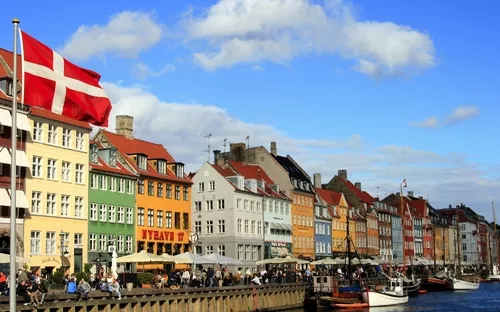 Bunte Häuserreihe am Nyhavn in Kopenhagen mit dänischer Flagge und Booten im Kanal.