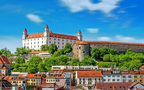 Burg auf einem Hügel mit roten Dächern und blauen Himmel im Hintergrund.