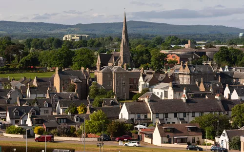 Ansicht eines Dorfes mit Kirche und Hügeln im Hintergrund, sonniger Tag.