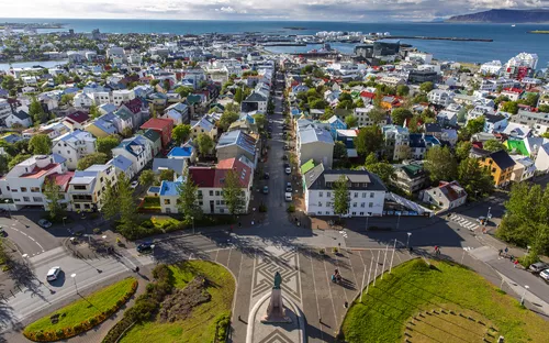 Blick auf die Küstenstadt Reykjavík mit bunten Häusern, Straßen und einem Hafen im Hintergrund.
