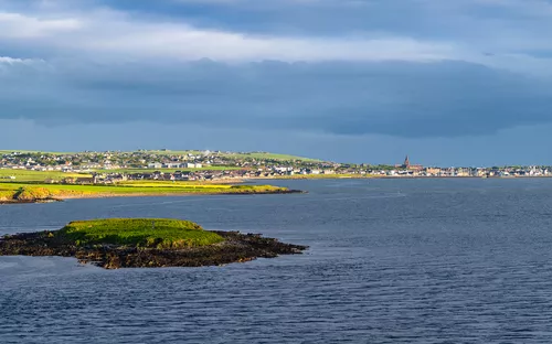 Insel im Meer mit Stadt im Hintergrund bei bewölktem Himmel