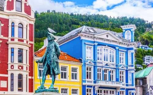 Statue mit Möwe, bunte Gebäude und bewaldeter Hügel im Hintergrund.