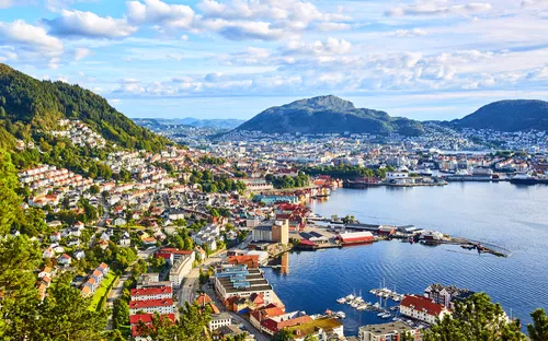 Stadtansicht von Bergen in Norwegen mit Bergen und Hafen unter blauem Himmel.