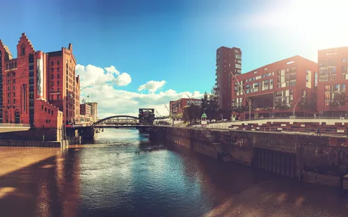 Stadtansicht mit historischen und modernen Gebäuden an einem Fluss bei Sonnenschein.