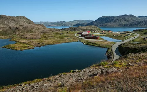 Fjordlandschaft mit See, Straße und kleinen Gebäuden unter klarem Himmel.