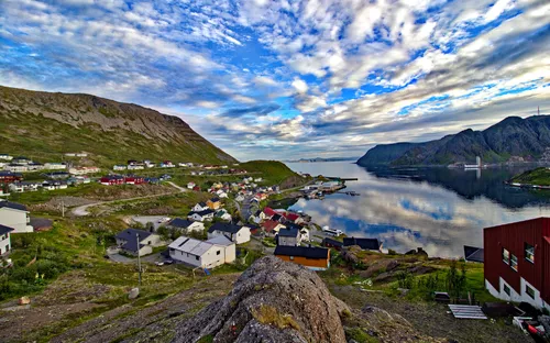 Küstenort mit bunten Häusern, Bergen und Wasser im Hintergrund bei bewölktem Himmel.