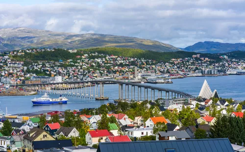 Küstenstadt mit Brücke, Schiff und Bergen im Hintergrund.