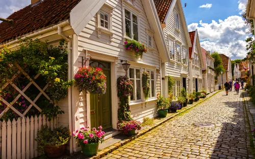 Gepflasterte Straße mit Blumen geschmückten weißen Holzhäusern bei Sonnenschein.