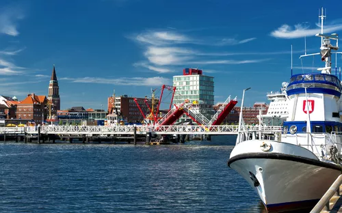 Hafenansicht mit Boot und Stadtpromenade unter blauem Himmel
