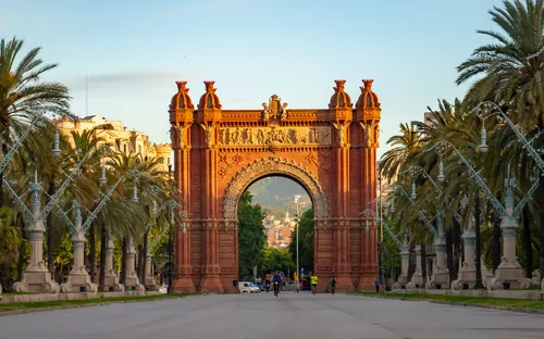 Triumphbogen in einer von Palmen gesäumten Promenade unter blauem Himmel in Barcelona, Spanien.