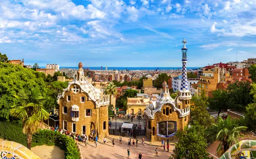 Blick auf den Park Güell in Barcelona mit historischem Gebäude und Menschen im Vordergrund.
