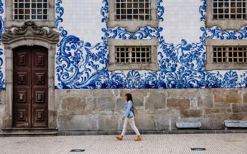 Person spaziert vor einer Fliesenfassade mit blauen Mustern.