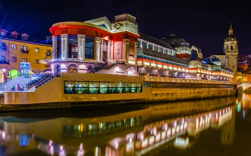 Nachts beleuchtete Stadtansicht mit Wasserreflektion und historischer Architektur.