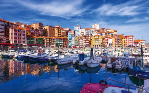 Bunte Gebäude und Boote in einem Hafen bei klarem Himmel.
