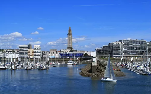 Hafen mit Segelboot, Gebäuden und Turm unter blauem Himmel.