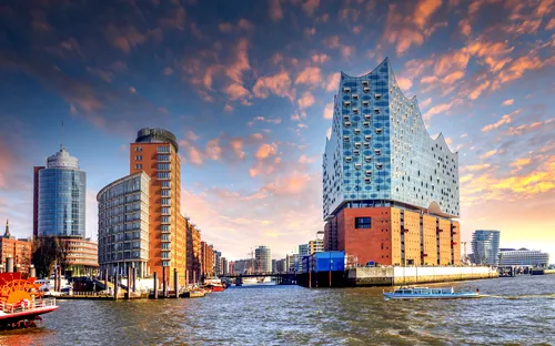 Elbphilharmonie in der Hafencity von Hamburg bei Sonnenuntergang mit Wasser im Vordergrund.