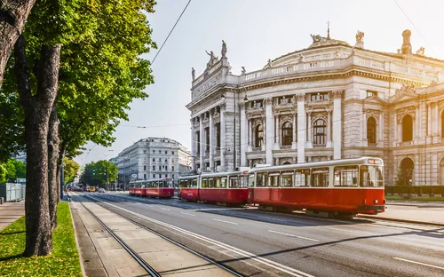 Wiener Ringstraße mit Blick auf das Burgtheater und eine vorbeifahrende rote Straßenbahn.