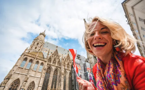 Lächelnde Frau mit österreichischer Flagge vor dem Stephansdom in Wien.