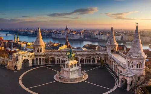 Blick auf den Fischerbastei-Komplex in Budapest mit der Donau im Hintergrund bei Sonnenuntergang.